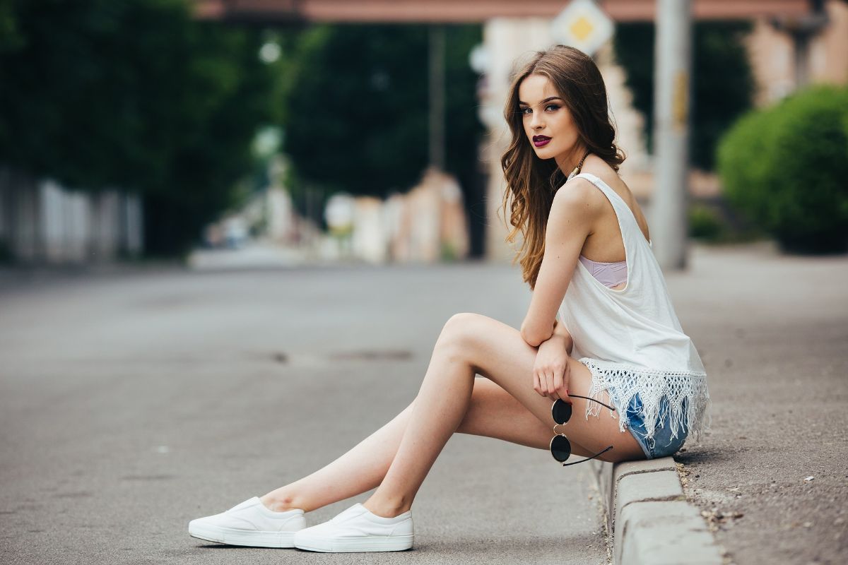 garota sentada em calçada usando roupas curtas e tênis branco